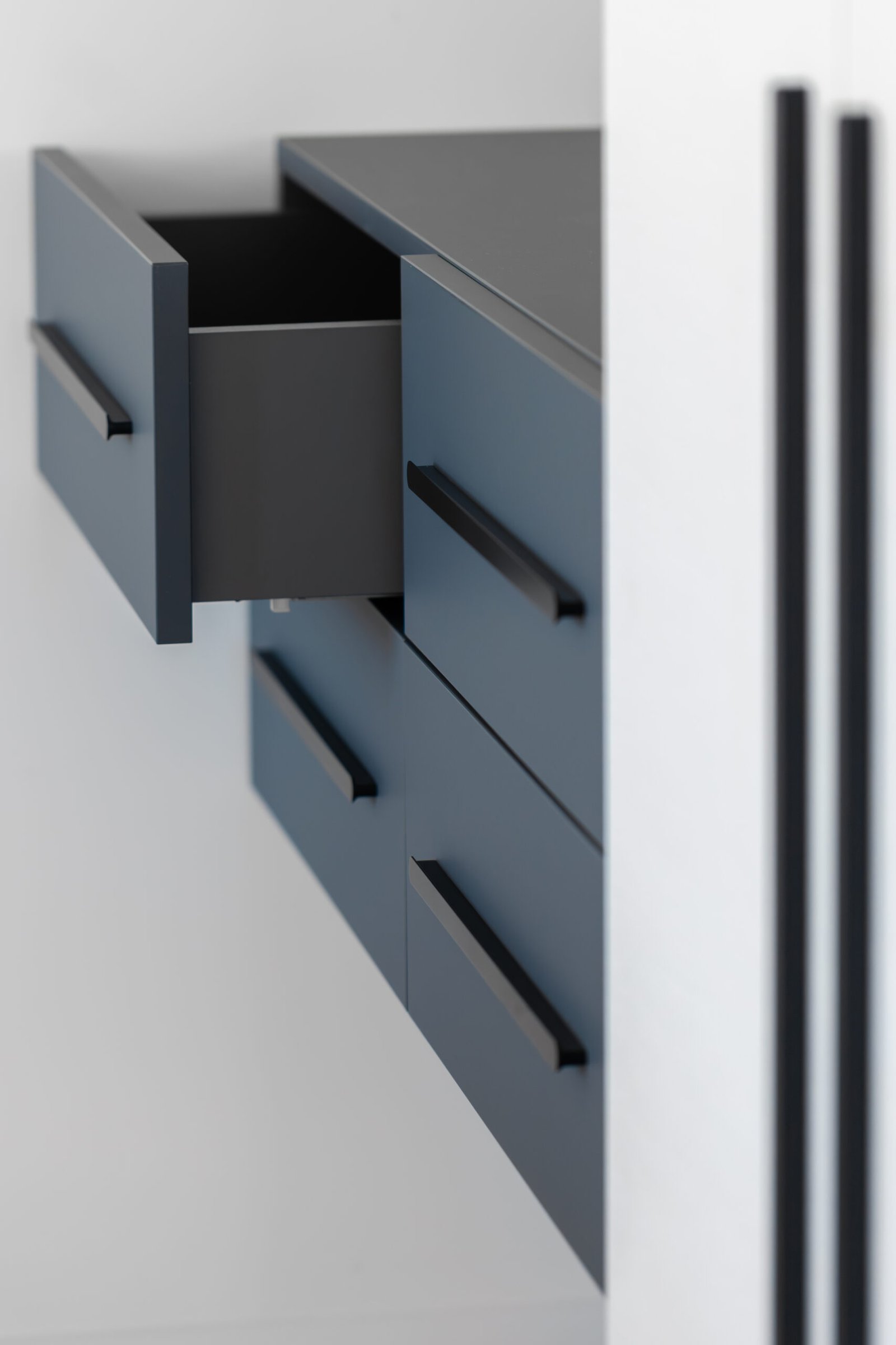 Side angle of a wall unit with matte blue fronts and an open top drawer. The white panel and black hardware create crisp contrast and a graphic, Scandic aesthetic.